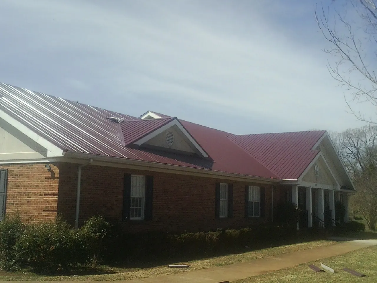 Red metal roof with gabled entries on a long brick building, from a Hail Damage Roof Repair job in Agawam