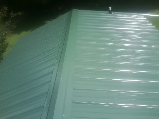 New green metal panels meeting at the ridge of a roof — Flat Roof Repair work by our crew in Agawam