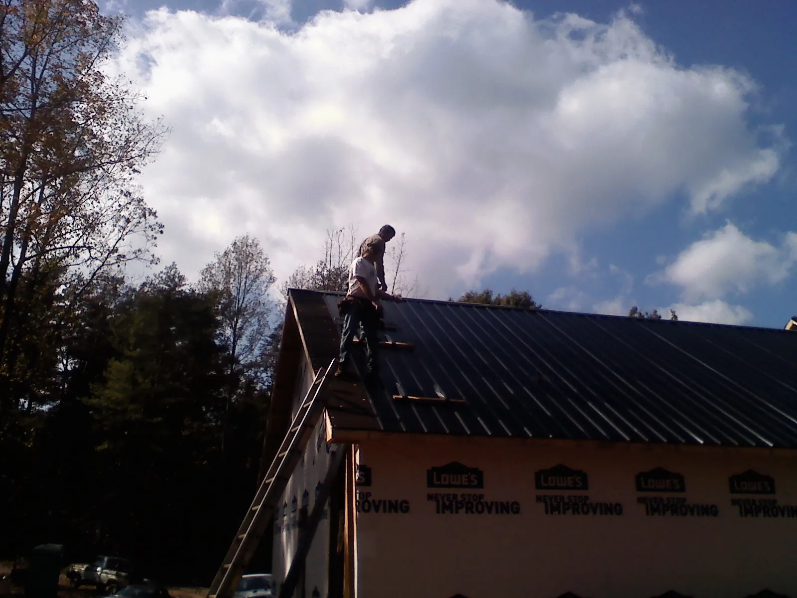 Roofer fastening dark metal panels high against a cloudy sky, from a Roof Inspection job in Agawam