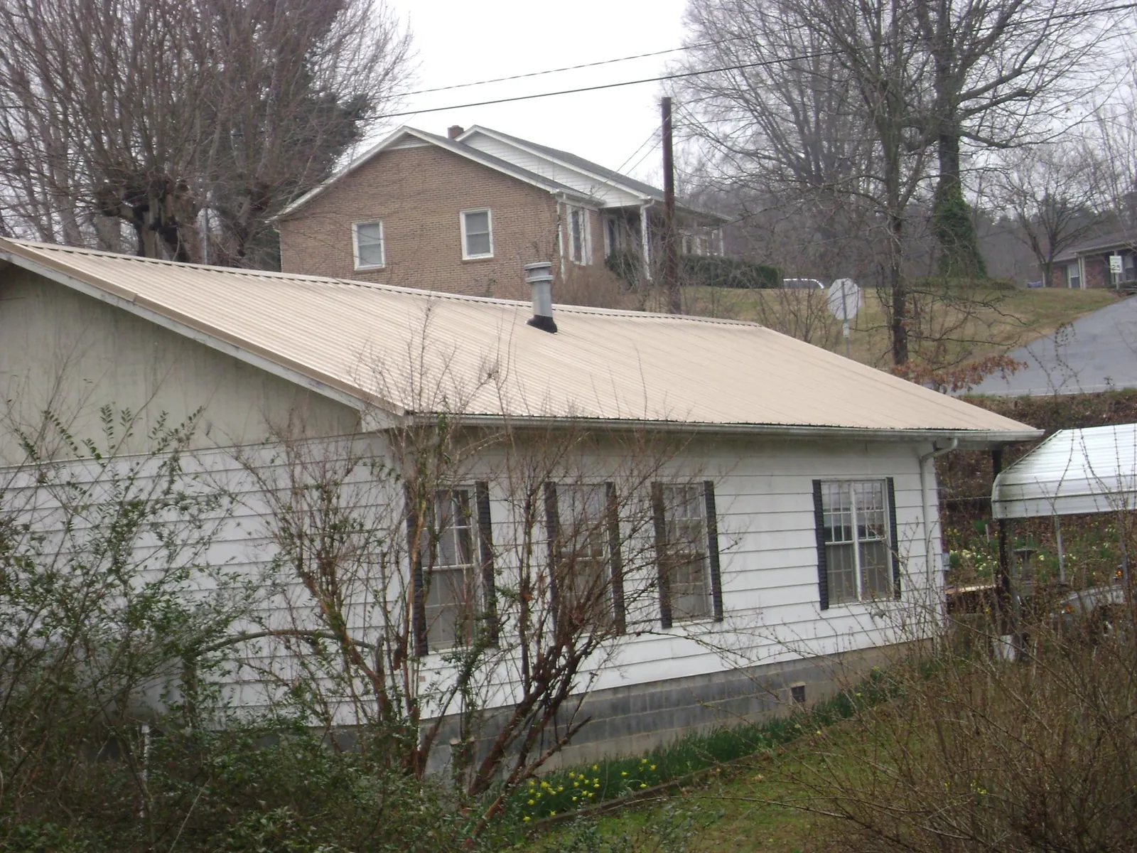 Tan metal roof on a white sided house set into a hillside — Commercial Roofing by Roofing Brothers in Agawam